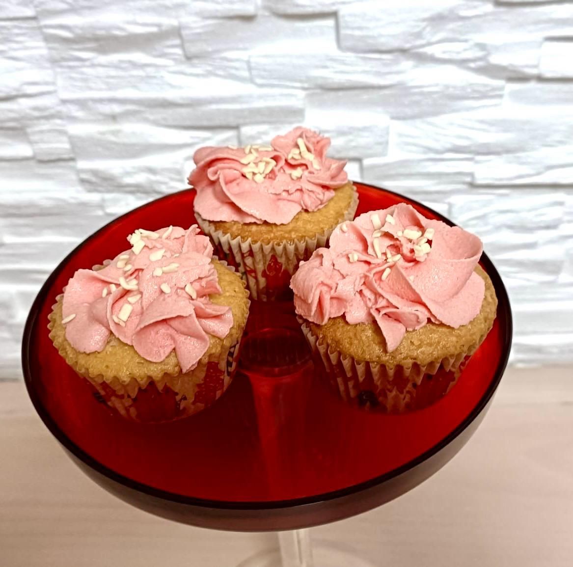 trois cupcakes avec de la crème rose sur une assiette rouge