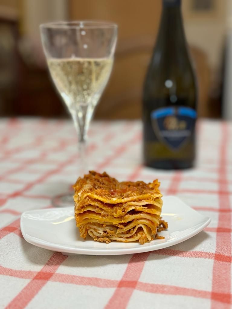 une assiette de lasagna est assise sur une table à côté d' un verre de vin .