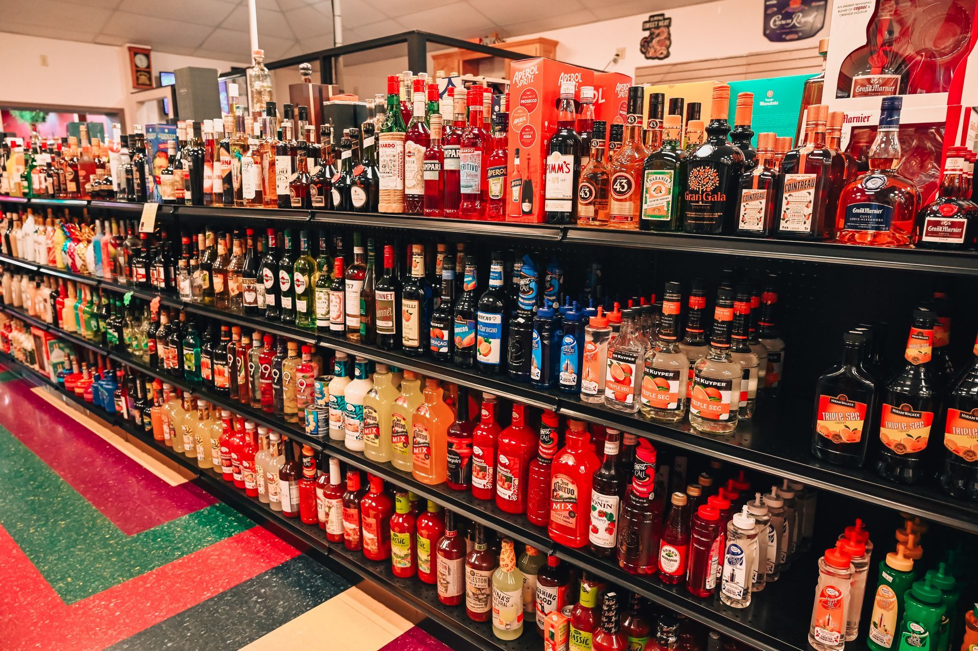 Shelves stocked with various liquor bottles inside a store, brightly lit, colorful floor.