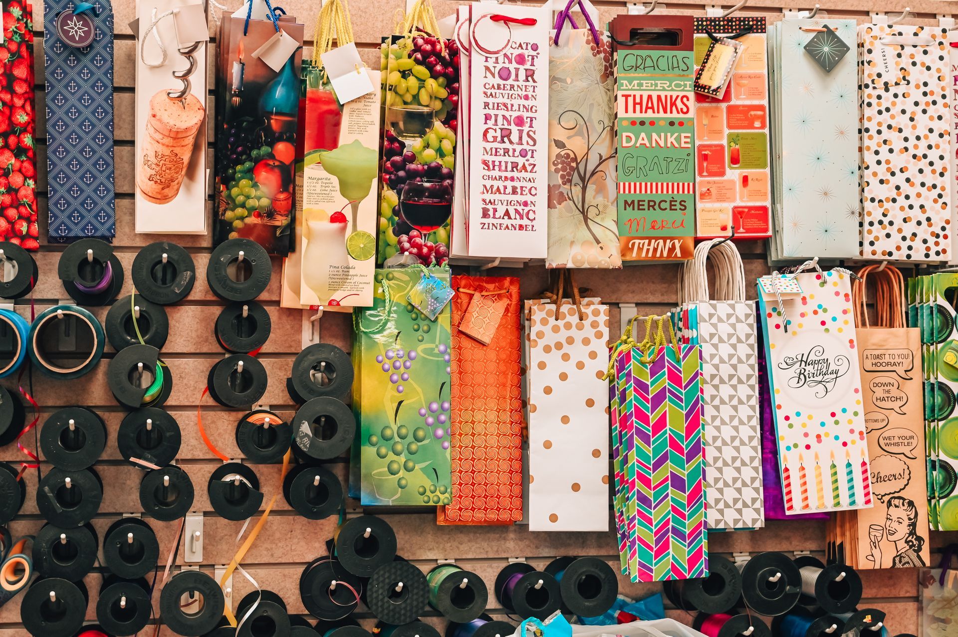 Wall display of colorful wine gift bags hanging with black bottle stoppers below.