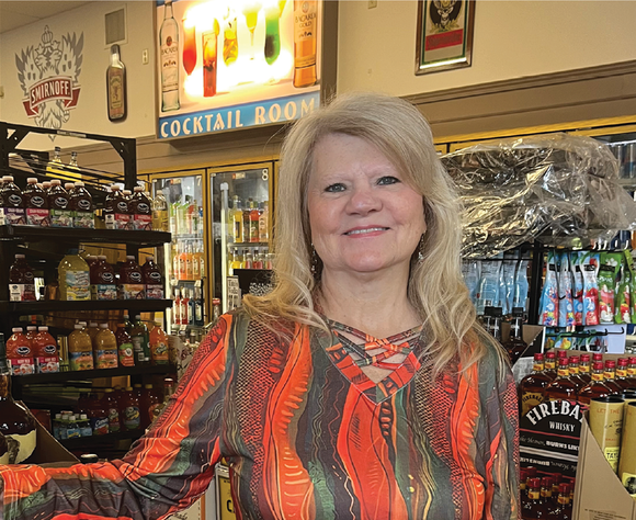 Woman in liquor store smiles, standing near shelves of products and a 