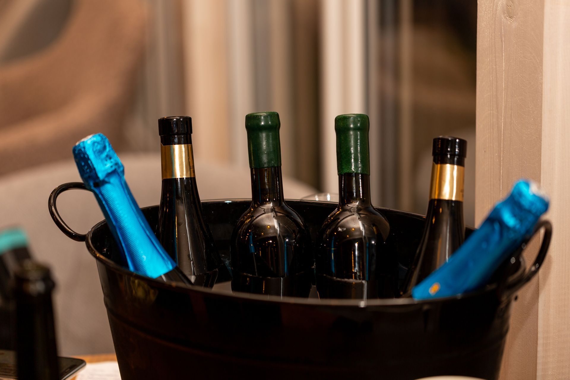 Black bucket holding several dark bottles with green and gold caps, and two bottles with blue foil.