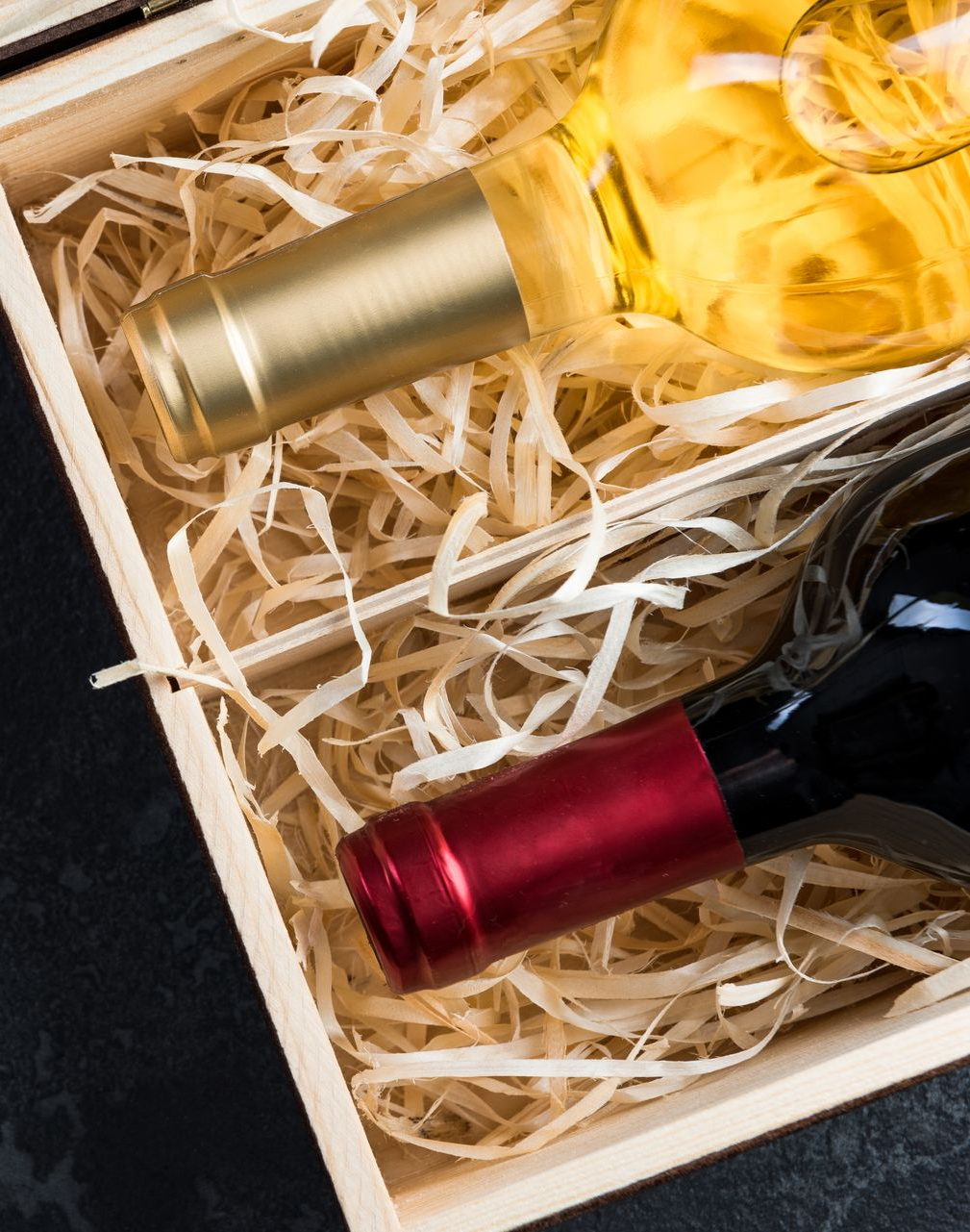 Wooden box with two wine bottles, red and gold caps, inside straw.