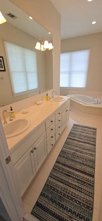 A bathroom with two sinks , a tub , a mirror and a rug.