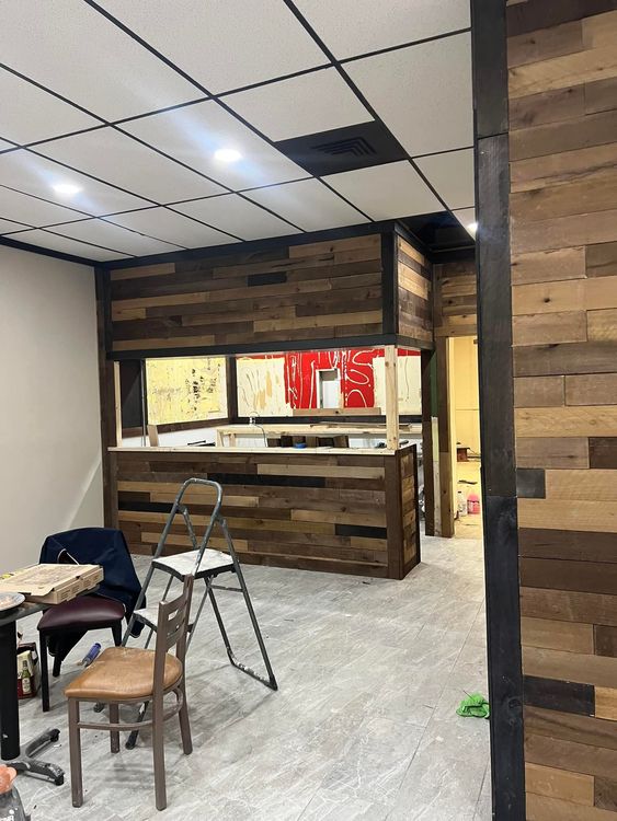 An interior space under renovation with wood-paneled walls, a service counter, a ladder, and a chair.