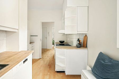 A bright, minimalist kitchen with white cabinets, light wood countertops, and hardwood flooring leading to a doorway.