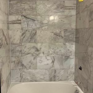 A white bathtub surrounded by large, rectangular, grey and white marbled wall tiles.