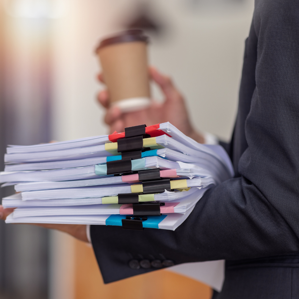 A man in a suit is holding a stack of papers and a cup of coffee.