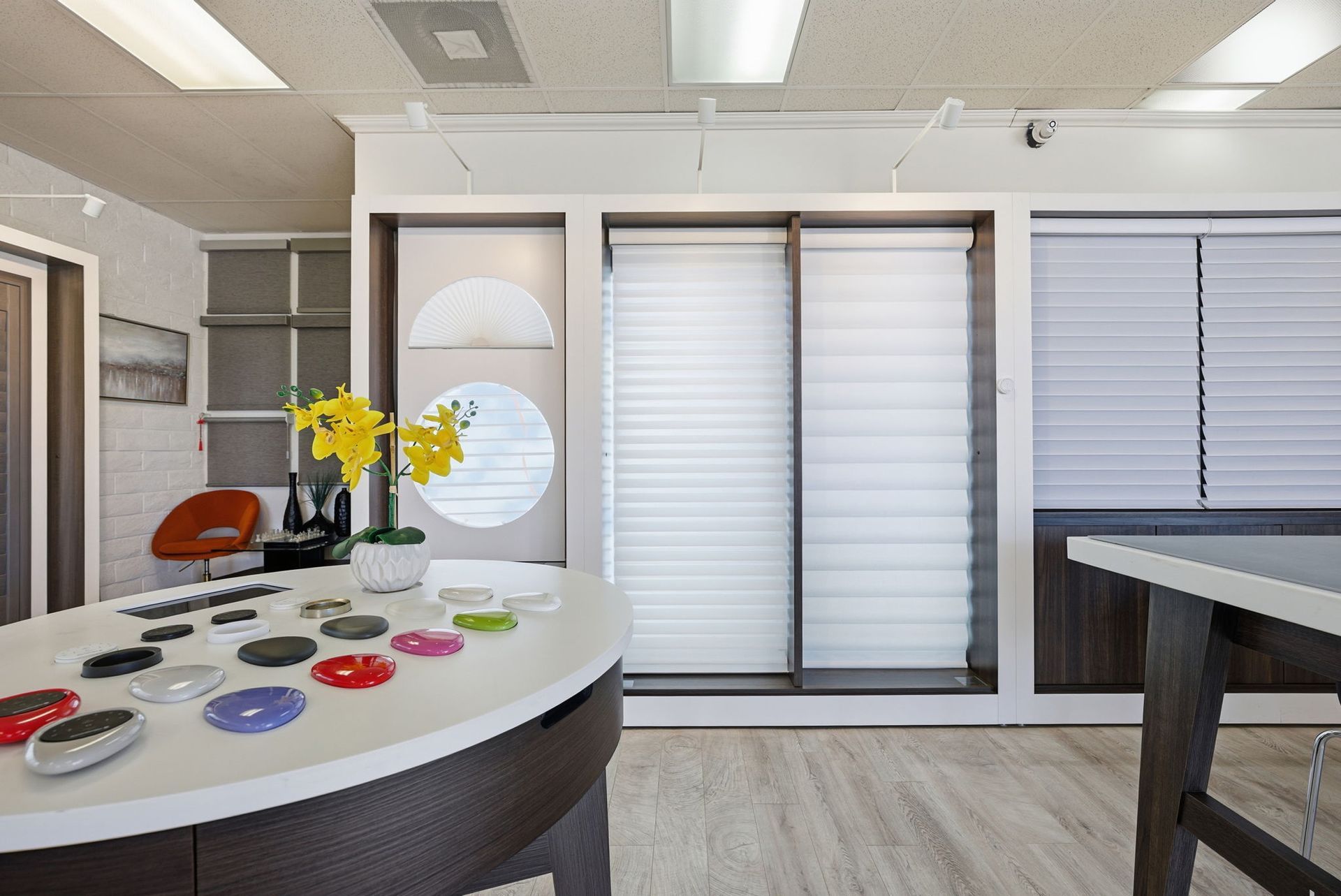 A modern showroom featuring various window blinds, display tables with color samples, and an orange accent chair.