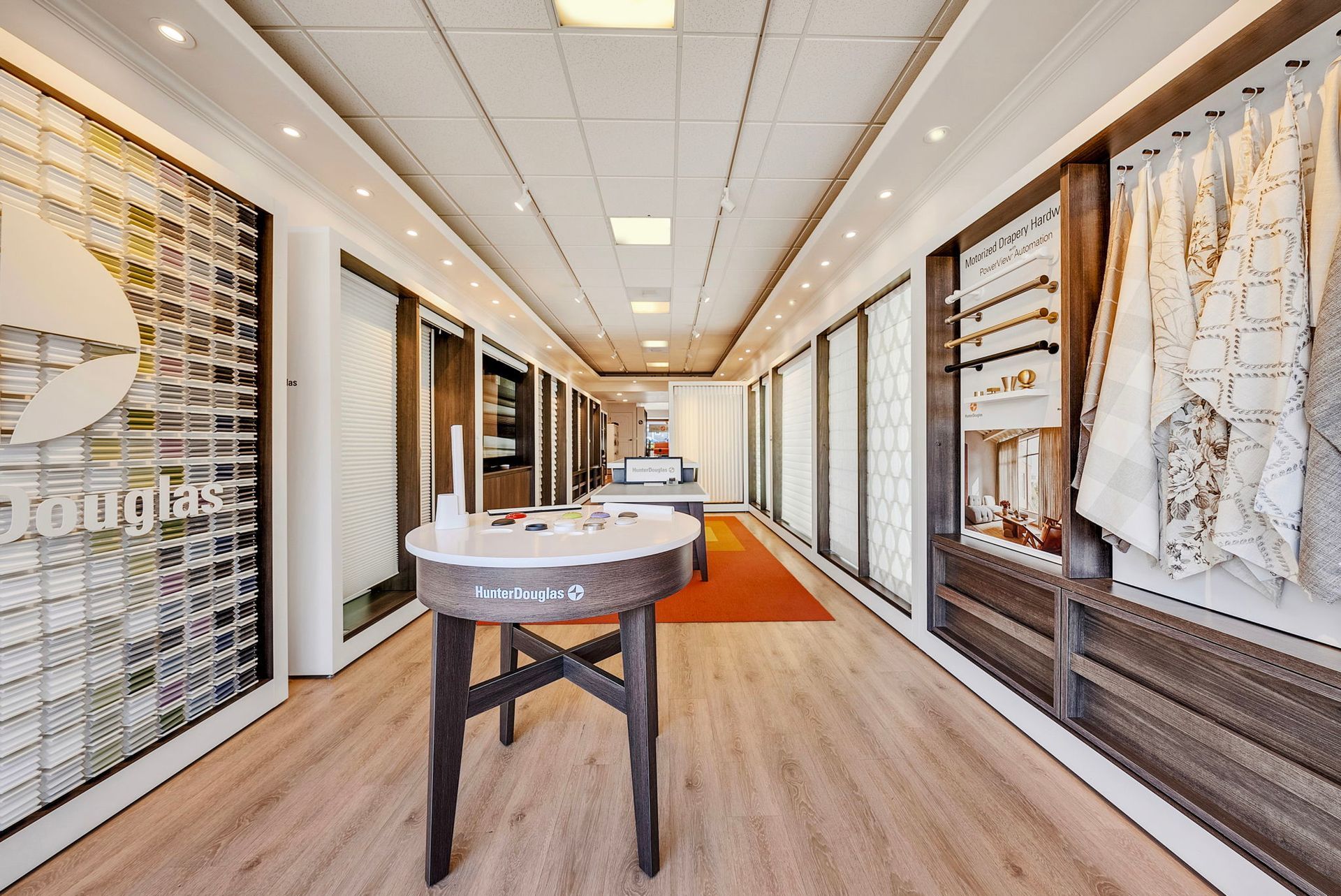 A brightly lit showroom featuring displays of fabric swatches, curtains, and a round wooden table in the center.