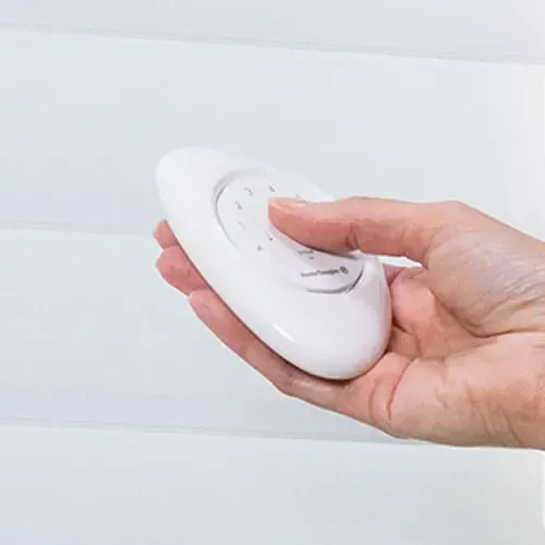 Hand holding a white, oval-shaped remote control with buttons.