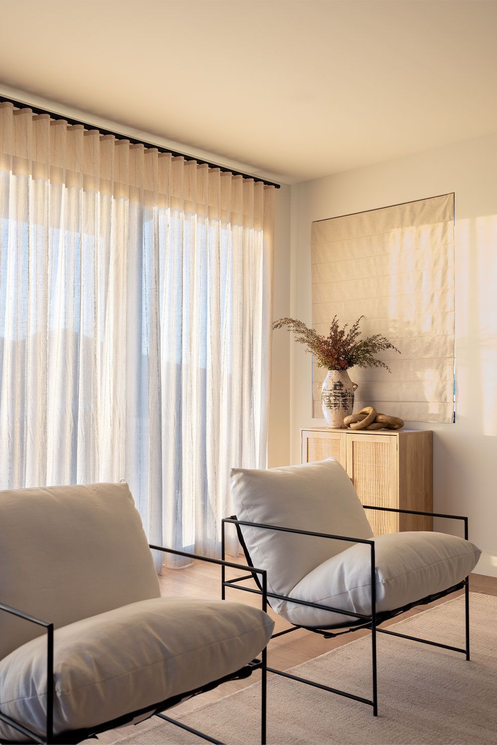 Two white armchairs with black metal frames face a window with ripplefold drapery.