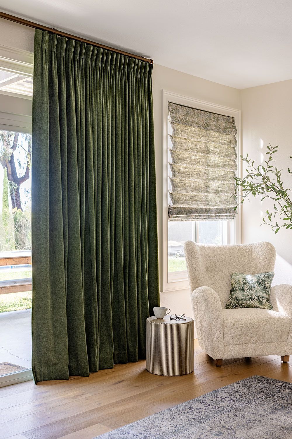Green velvet curtains frame an open doorway. A window with a patterned shade, and a cream armchair complete the scene.