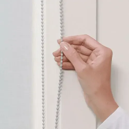 A hand pulling a beaded chain, likely for a window blind.