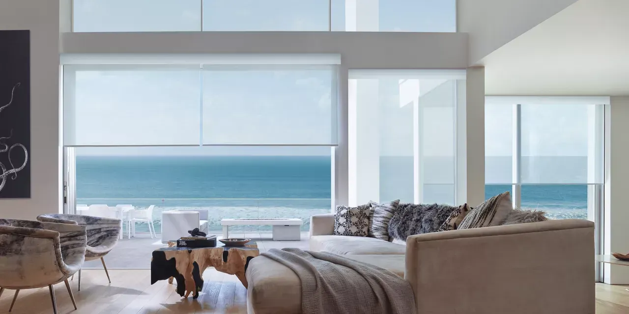 Living room with ocean view, white walls, modern furniture, and roller shades.