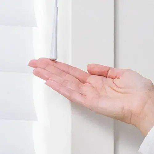 Hand holding a white cord, possibly for a window blind, near a white shutter.