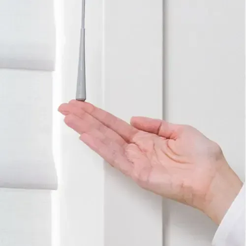 Hand pulling down a gray cord attached to a white window blind.
