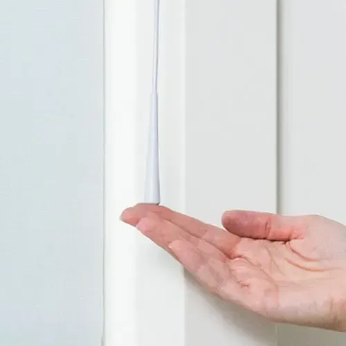 Hand reaching towards a white pull cord hanging from a white door frame.