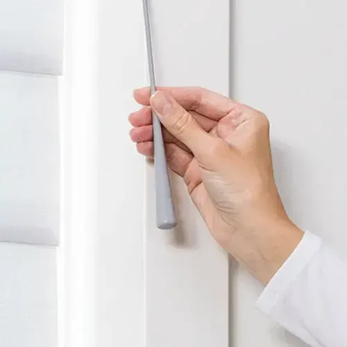 Hand pulling a gray wand to adjust white window shutters.