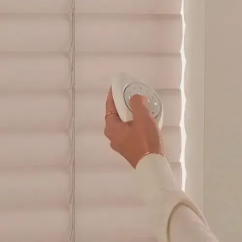 Hand holding a white remote, adjusting white window shutters.