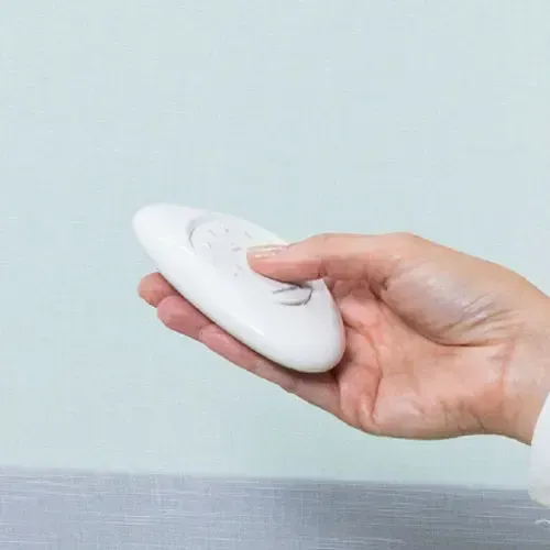 Hand holding a white, oval-shaped remote control against a light blue background.