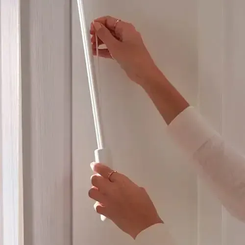 Person's hands pulling a white wand to open window blinds in a white room.