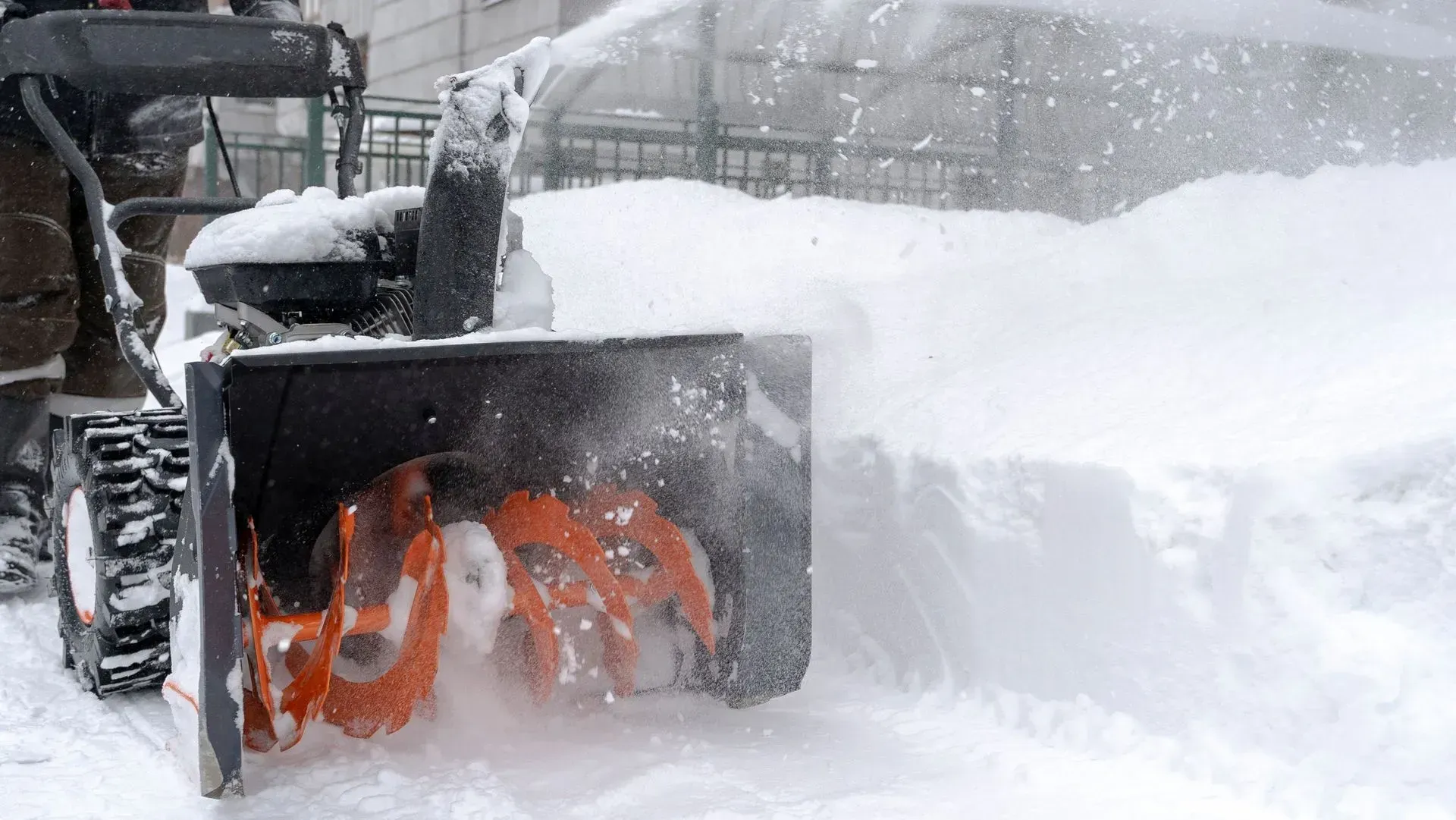 Snowblower clearing deep snow on a driveway, throwing white snow to the side.