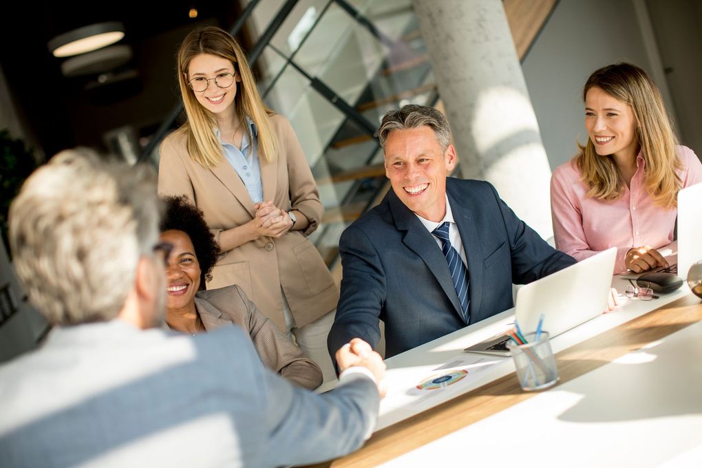 Business meeting around a conference table, with one person shaking hands and others smiling.