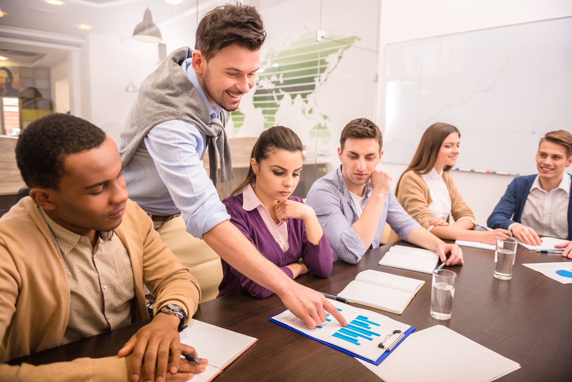 Coworkers gathered around a table reviewing charts and a tablet during a meeting