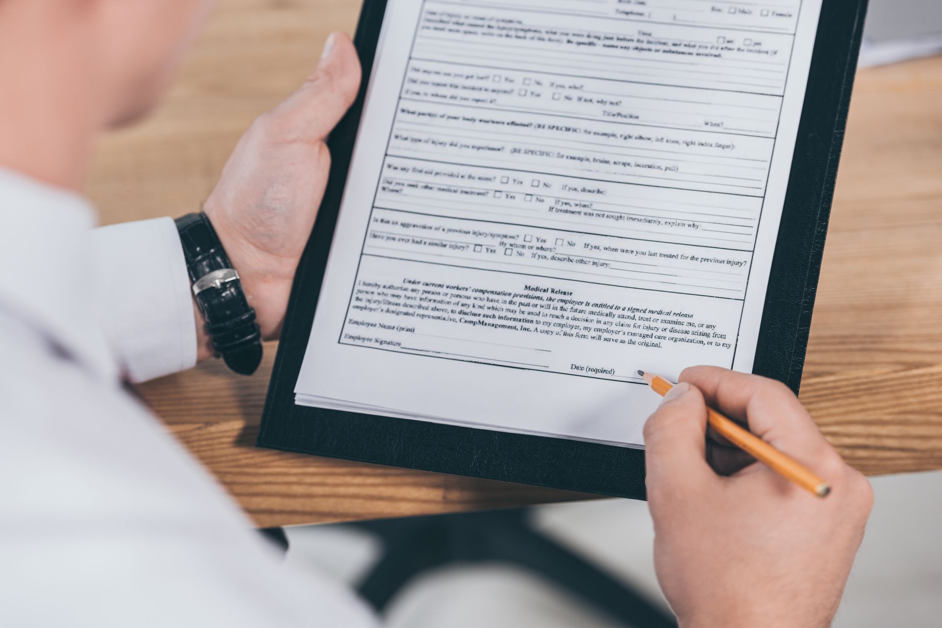 Person signing a document on a clipboard with a pencil at a wooden table