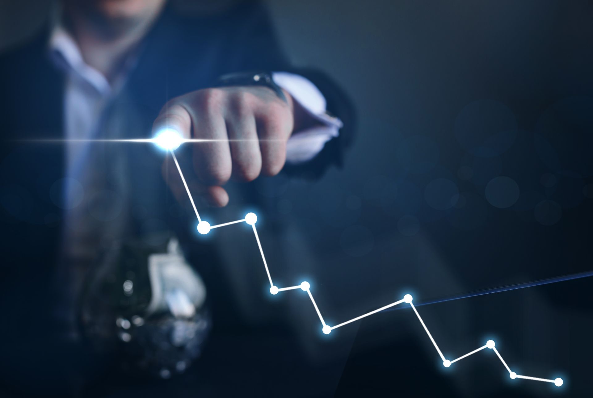 Businessman pointing at a glowing downward line graph on a dark blue screen
