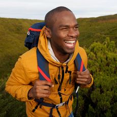 Smiling hiker in a yellow jacket with a blue backpack trekking through green hills