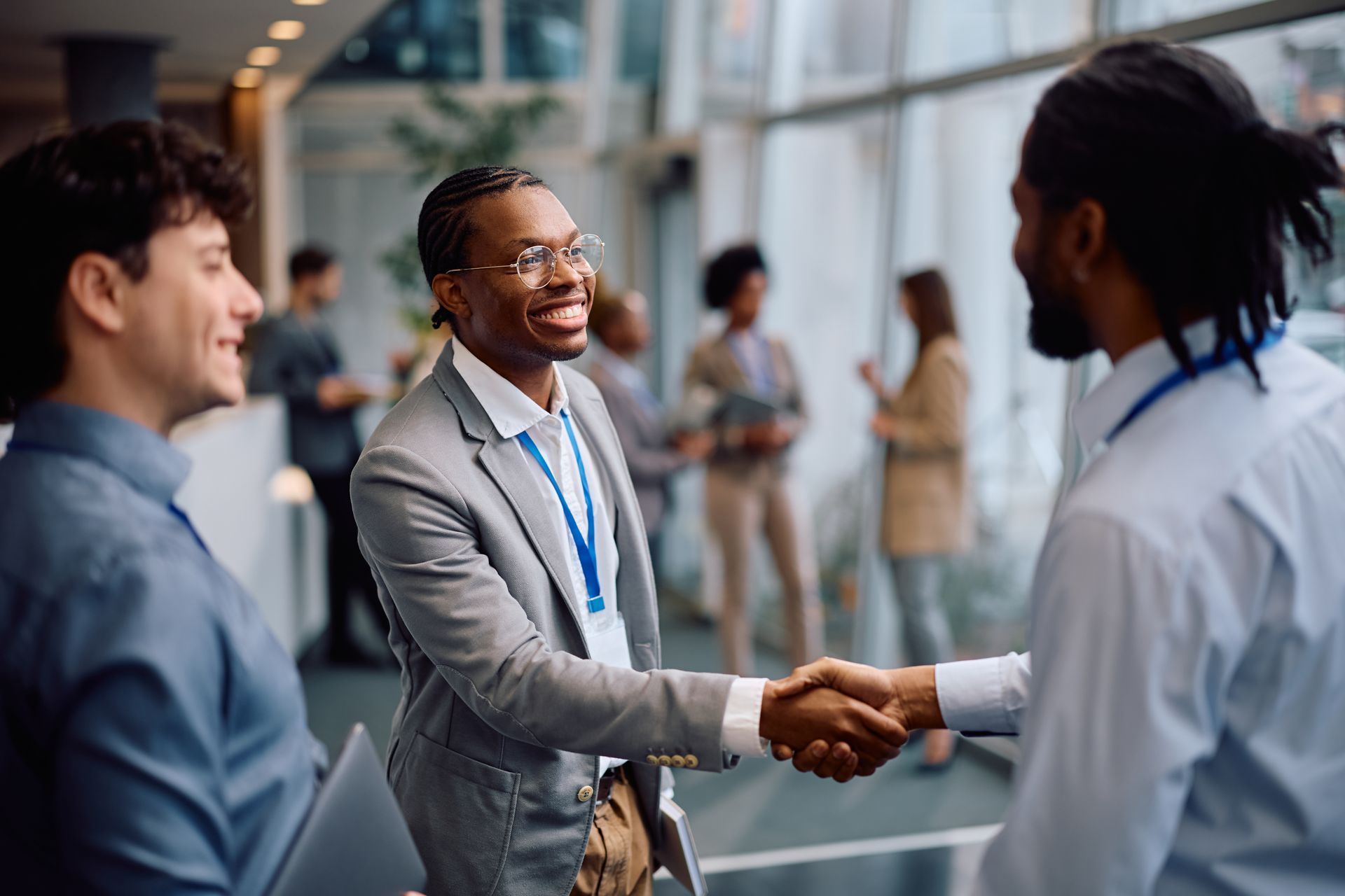 Three people shaking hands in a bright office lobby during a professional meeting.