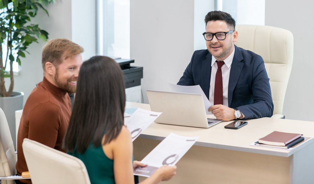 Three people meeting in a bright office with a man in a suit speaking across a desk