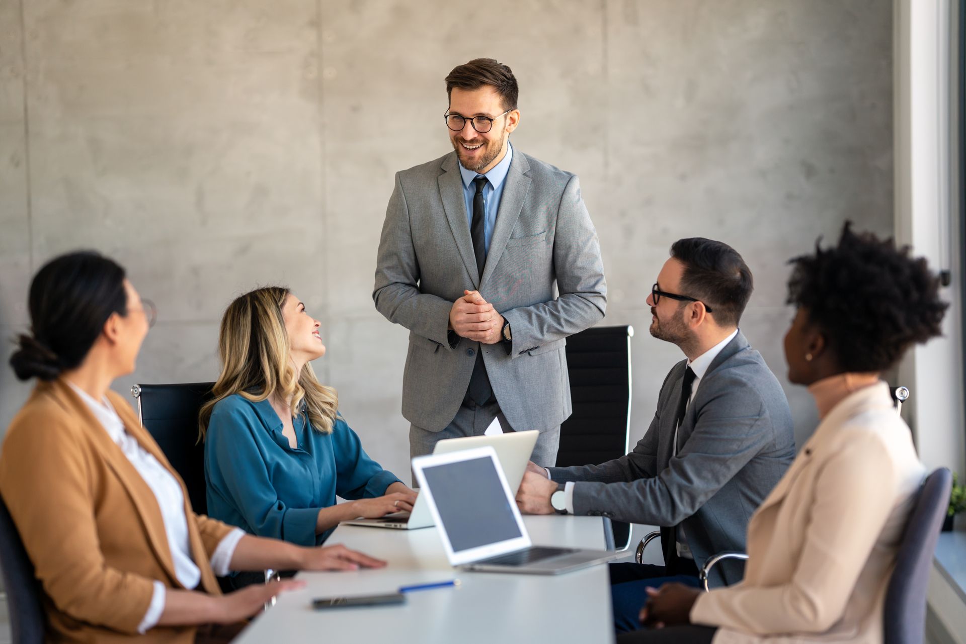 Business meeting with five people gathered around a conference table as a man presents at the front