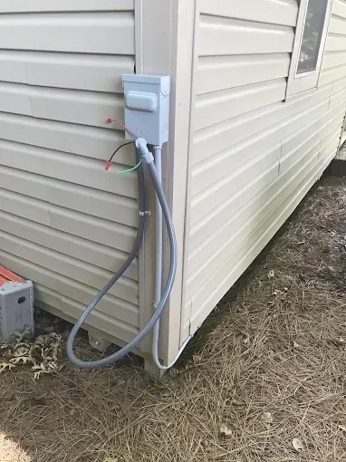 Outdoor electrical box and conduit attached to a beige sided structure, near a window.