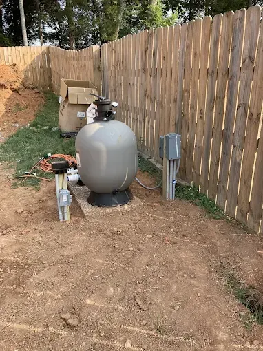Pool filter equipment near a wooden fence, on a dirt and grassy area.