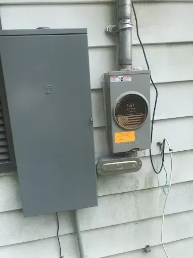 Gray electrical box and meter attached to a light-colored building's siding.