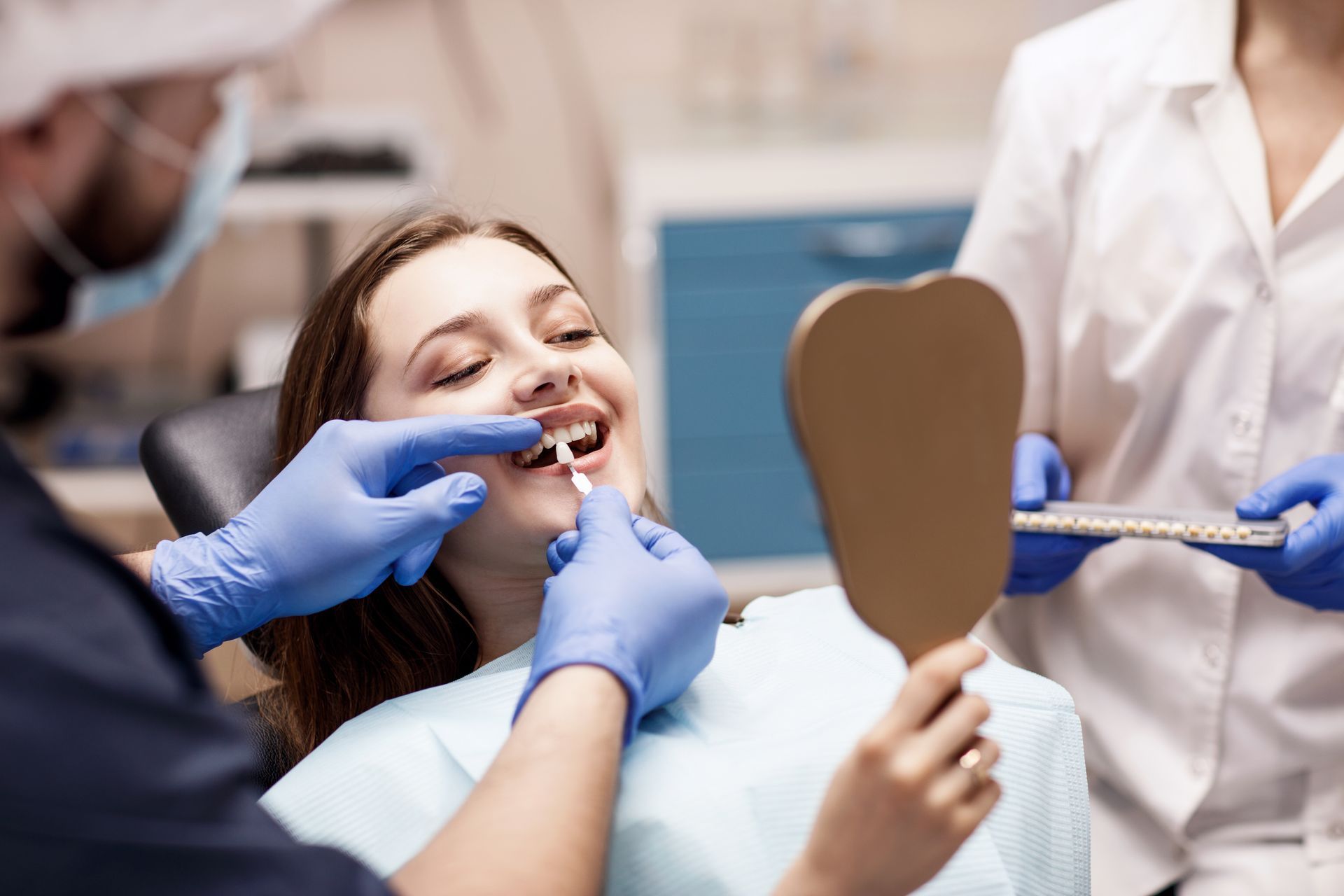 A female patient is being shown teeth shades with samples by a dentist and dental assistant.