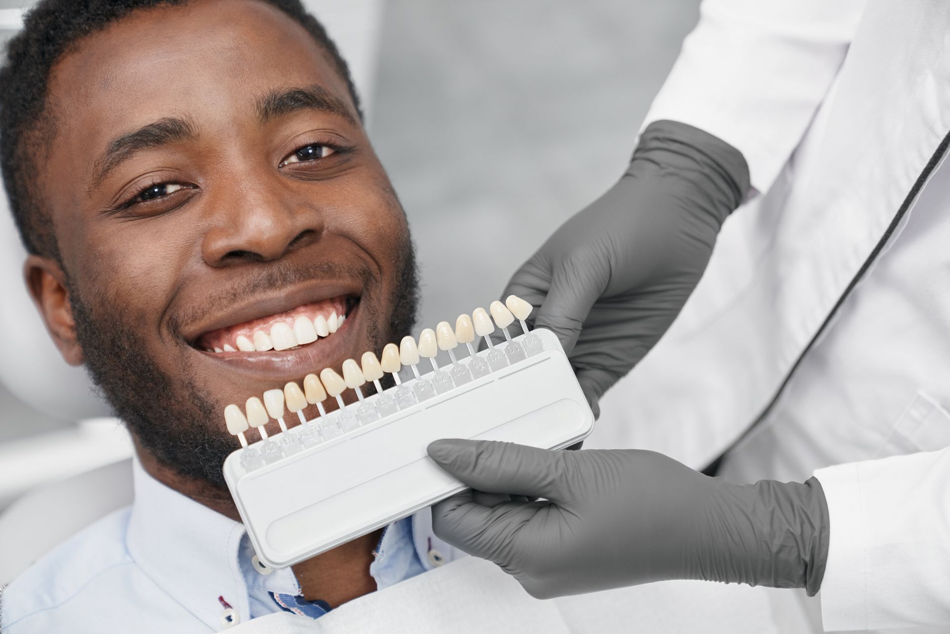 Man smiling while a cosmetic dentist keeps a range of veneers.