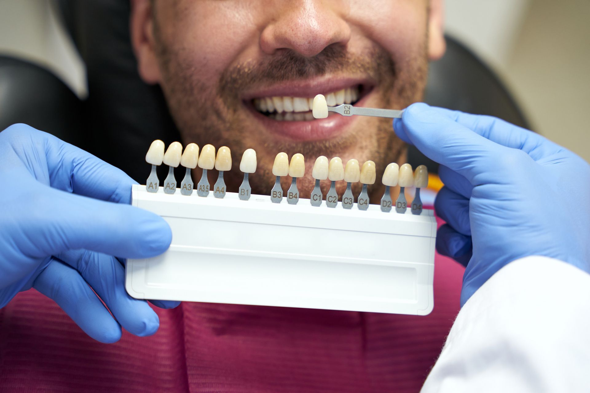 Dentist comparing tooth shade with a guide, patient smiling in dental chair. Dentist comparing tooth shade with a guide, patient smiling in dental chair.