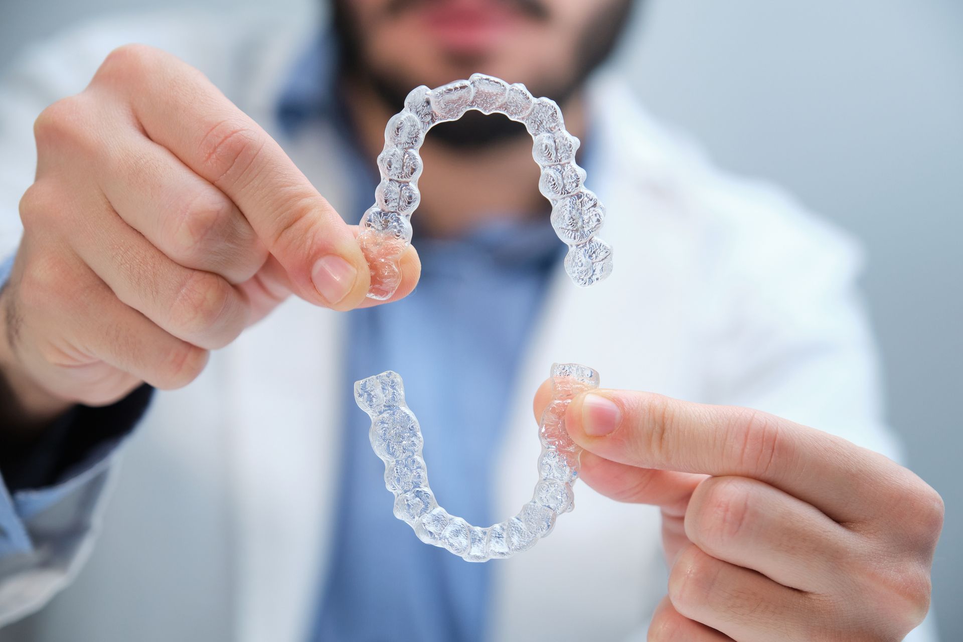 Cosmetic dentist in the background holding Invisalign aligners.