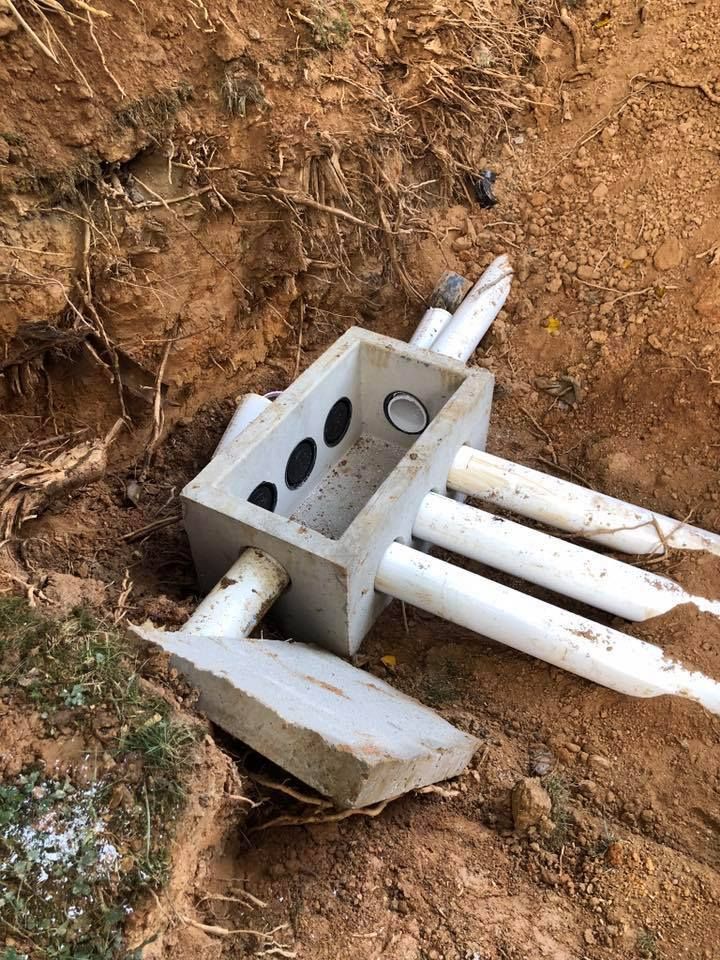 Concrete electrical junction box with white PVC pipes in a dirt excavation.