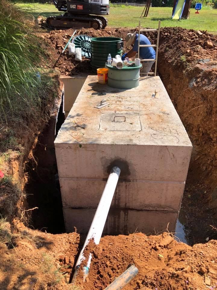 Concrete septic tank being installed in a dirt trench; worker nearby.