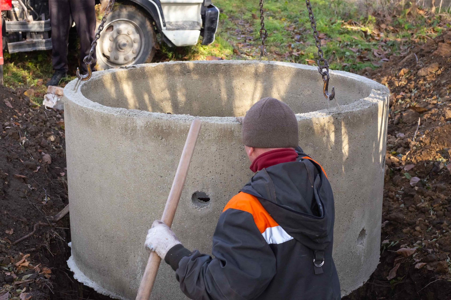 Man with shovel near concrete well ring being lowered by a chain into the ground.
