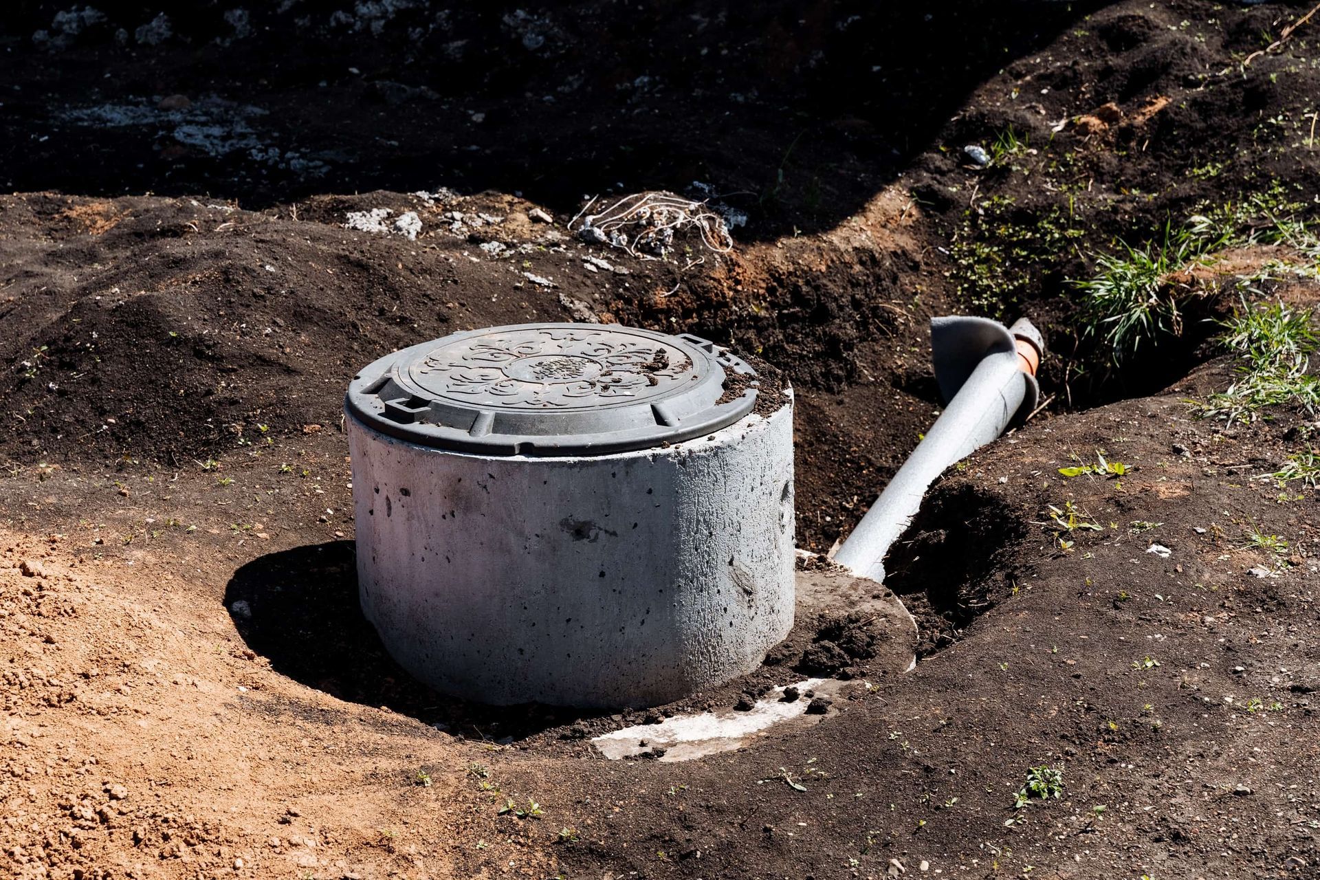 Concrete septic tank with lid, partially buried, near a pipe and dark soil.