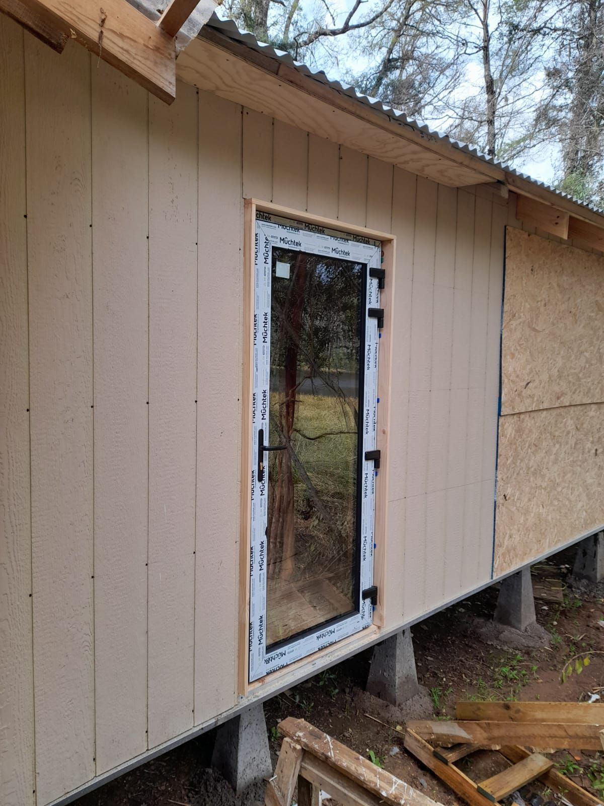Exterior de un edificio con puerta de vidrio, revestimiento de color claro y marco de madera.