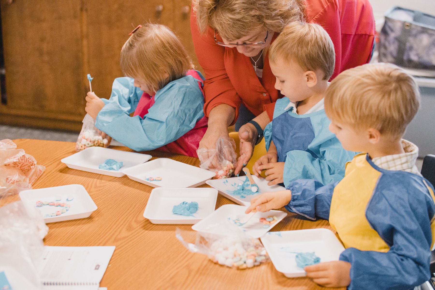 Children and adult painting with blue paint at a table; inside.