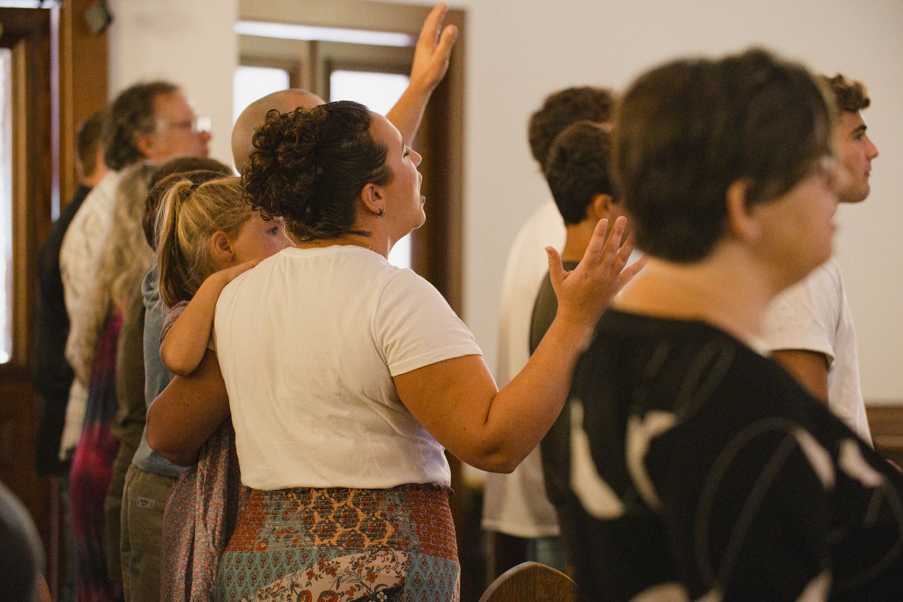 People with arms raised in prayer or praise, inside a light-filled church.