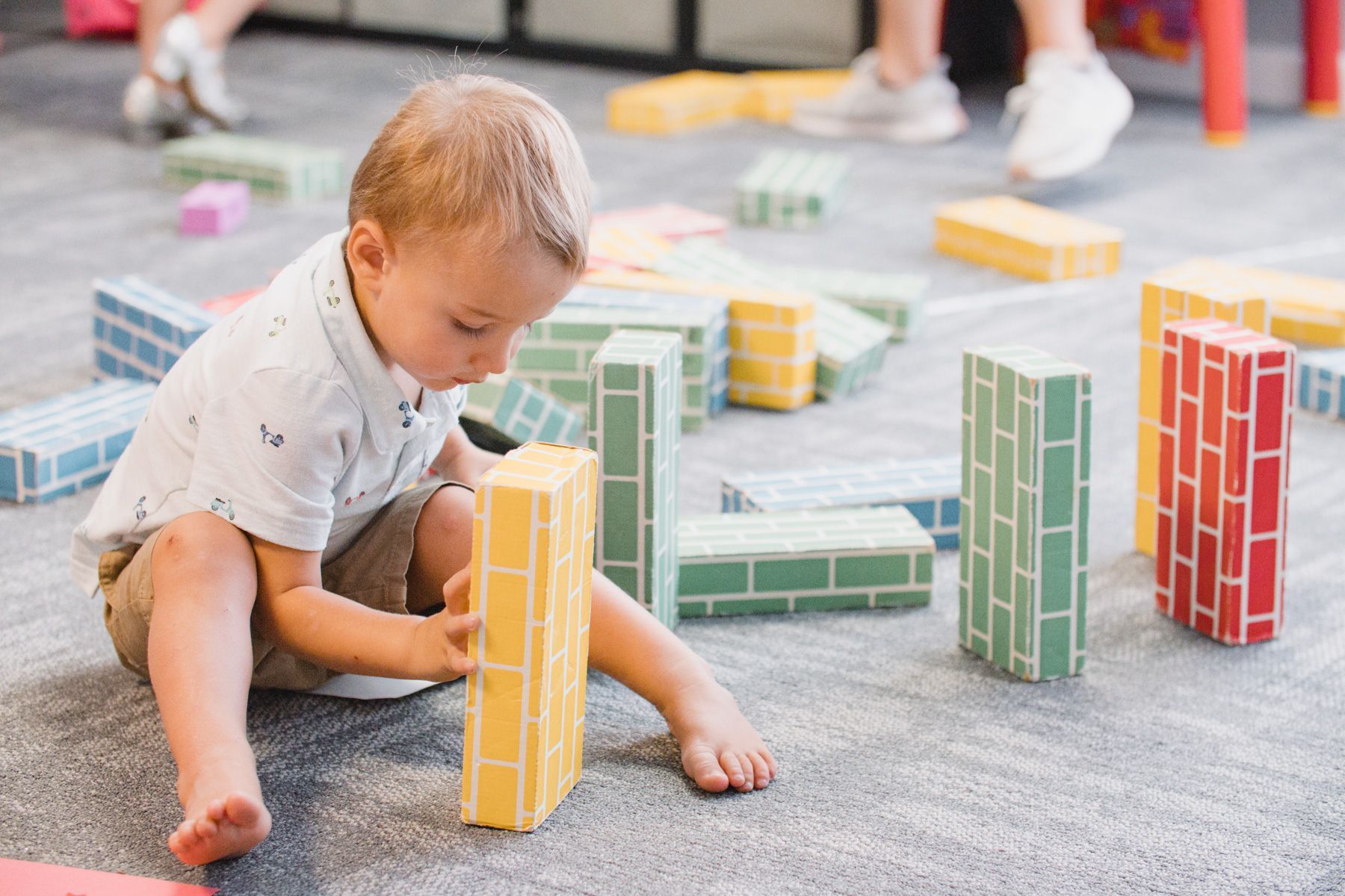 Boy sitting on the floor plays with colorful brick blocks.